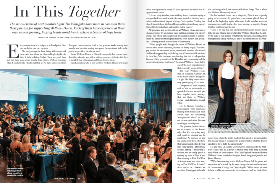 A large ballroom event with elegantly set tables full of guests, floral centerpieces, and three women posing together on stage beside a blue “WELLNESS” sign.
