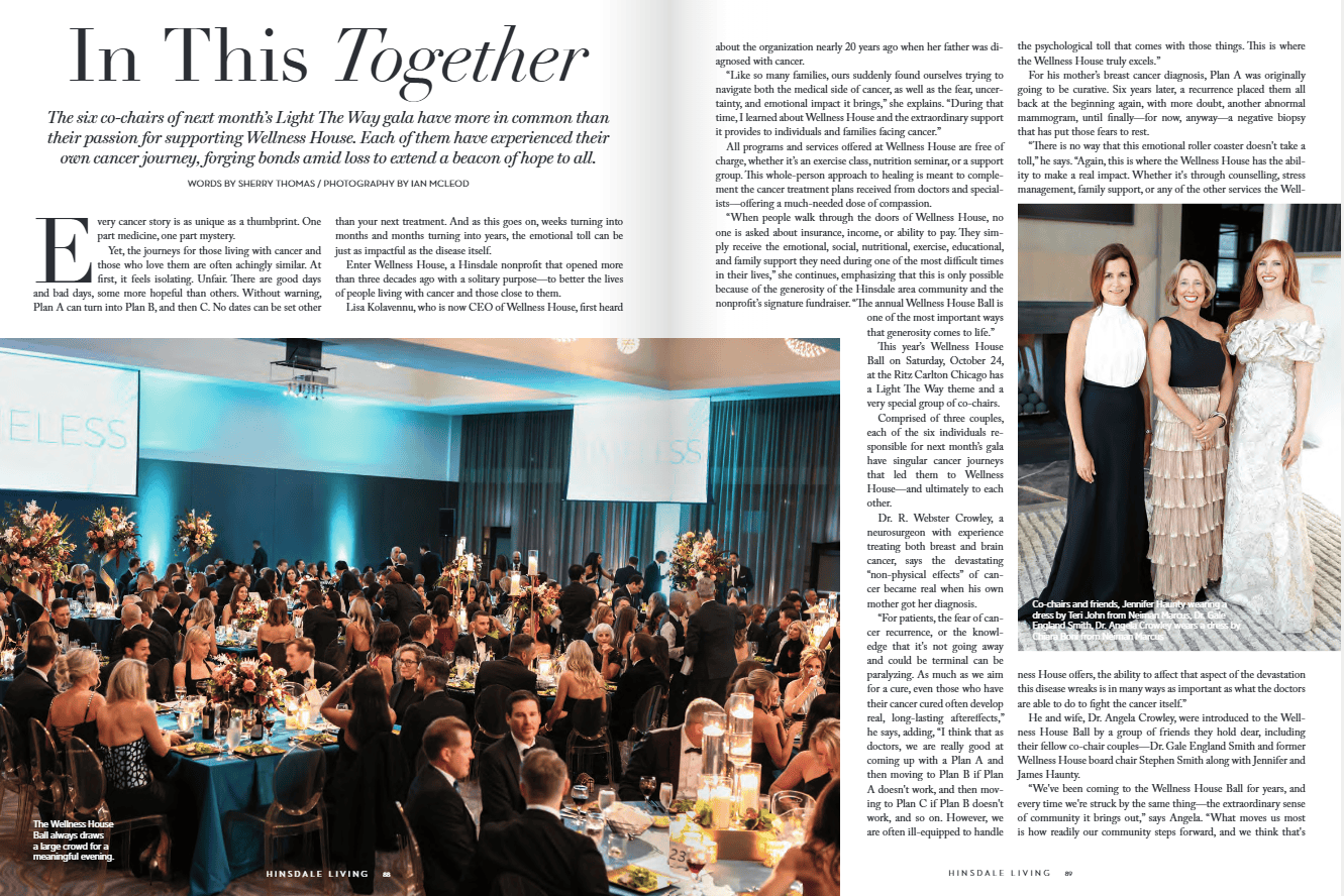 A large ballroom event with elegantly set tables full of guests, floral centerpieces, and three women posing together on stage beside a blue “WELLNESS” sign.